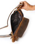 Brown leather handbag held open by a hand on a white background