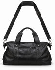 Modern black full-grain leather duffel bag with its adjustable shoulder strap raised above.