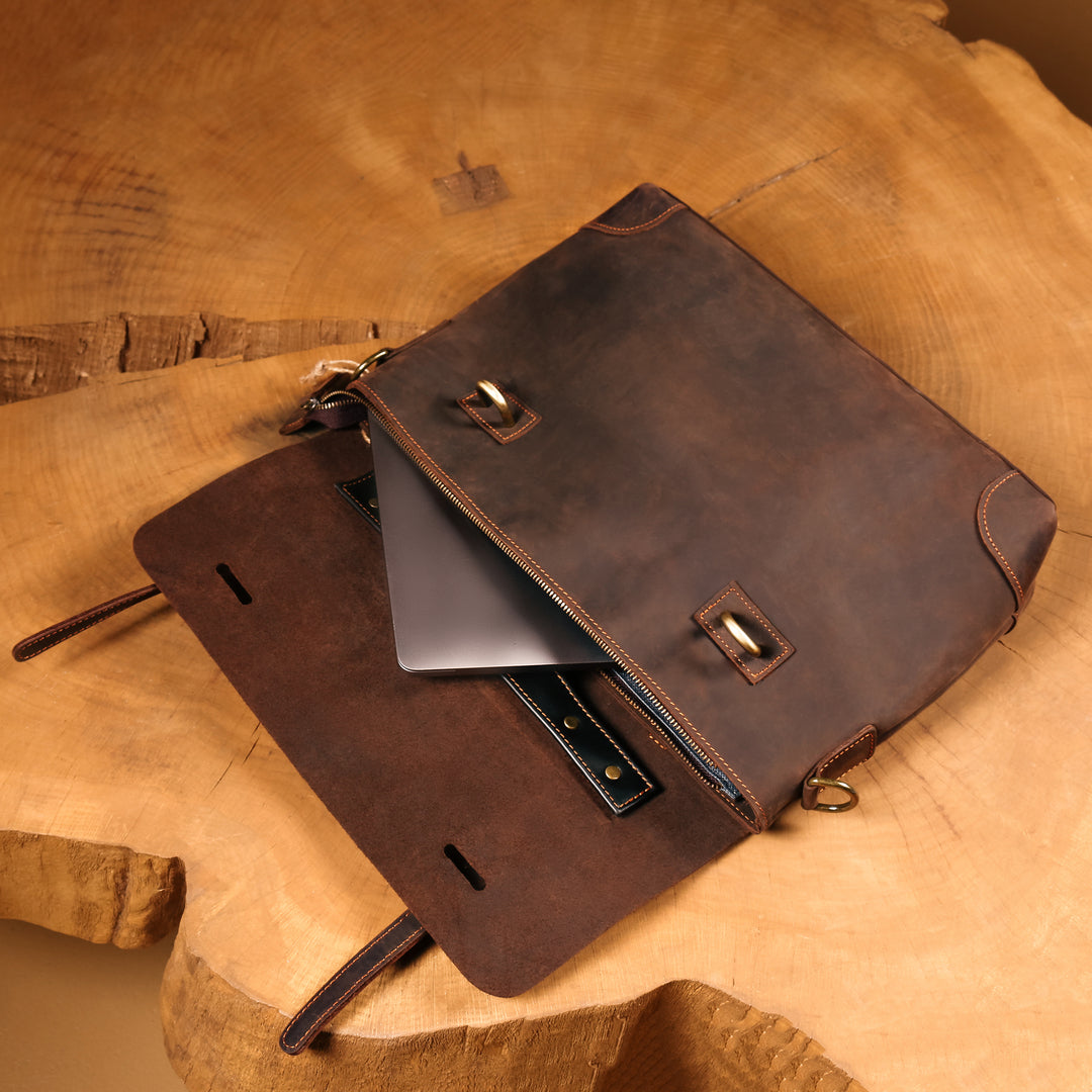 Open vintage leather bag showing compartments for a laptop, charger, and documents.