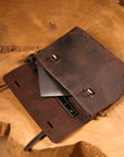 Open vintage leather bag showing compartments for a laptop, charger, and documents.