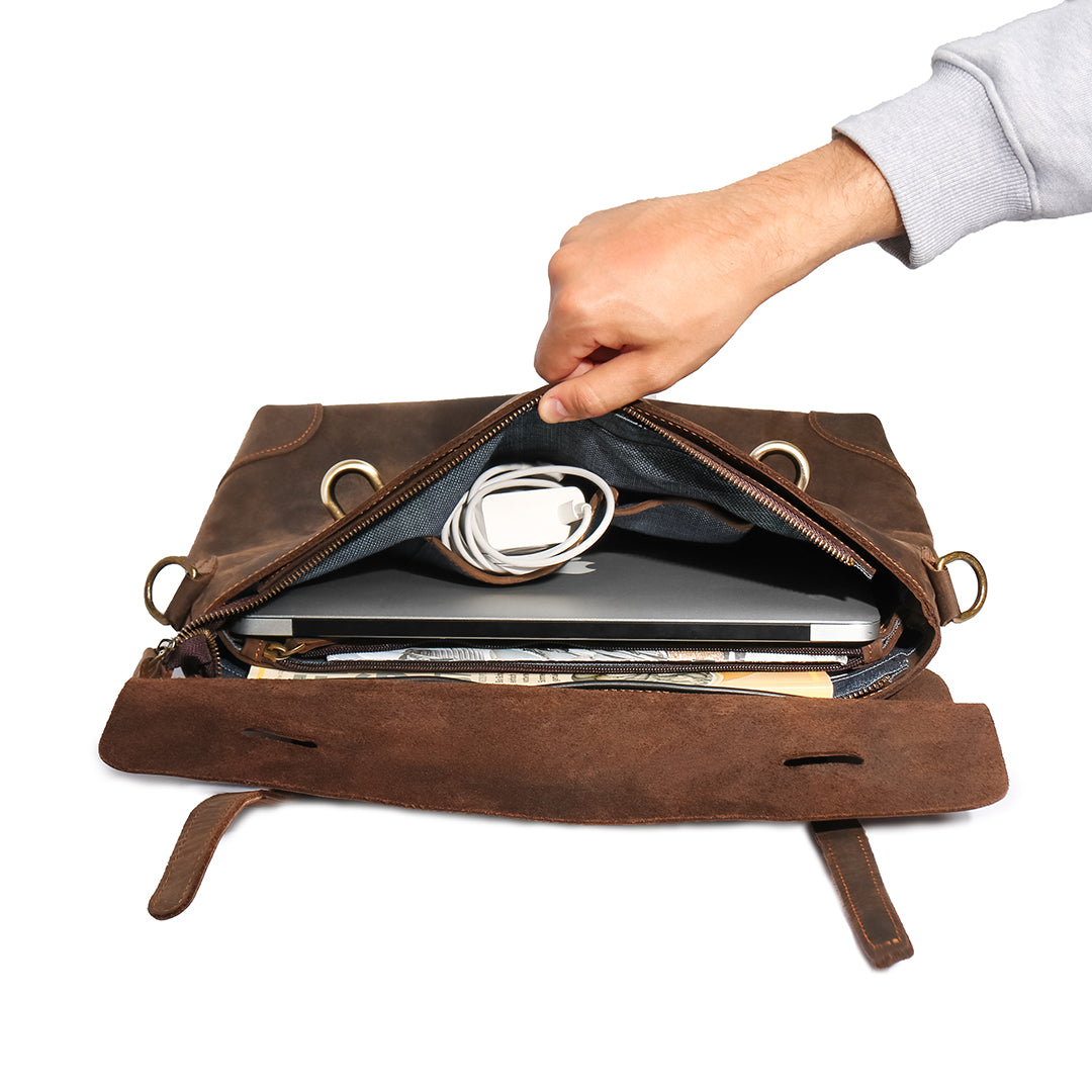 Hand opening a vintage leather messenger bag, showing its spacious interior with compartments for laptop and accessories.