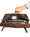 Hand opening a vintage leather messenger bag, showing its spacious interior with compartments for laptop and accessories.