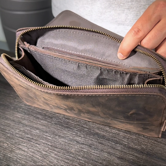 Detailed view of a dark brown men's leather clutch on a wooden table, showcasing its elegant design and Crazy Horse leather.