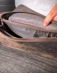 Detailed view of a dark brown men's leather clutch on a wooden table, showcasing its elegant design and Crazy Horse leather.