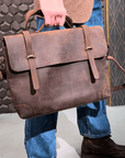 A man in classic attire modeling a handmade vintage leather briefcase and messenger bag, showcasing versatility.