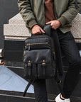 Professional black leather backpack for men with two front buckle pockets, upper zipper compartment and padded shoulder straps