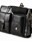A black leather briefcase has one front flap pocket open, revealing its dark underside and round magnetic snap.