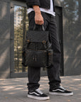 Quilted black leather travel backpack for men with buckle flap, front zip pocket, side pockets and top carry handle