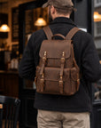 Rugged brown leather backpack for men with buckle straps, large front pocket, side pockets and top carry handle