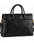 A black full-grain leather briefcase is shown at a slight angle with rolled handles, a rounded flap and a wide front slip pocket.
