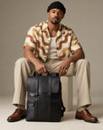 Sleek black leather backpack for men with structured flap closure, front zipper pockets and top carry handle