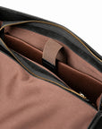 The open black full-grain leather briefcase reveals a brown sleeve with a retaining strap and a black leather end tab.