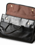 The black full-grain leather briefcase has its flap lifted to reveal brown lining and two magnetic snap closures.
