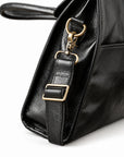 A close-up of the black full-grain leather briefcase shows the brass-tone swivel clasp, D-ring and stitched strap attachment.