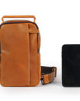 Compact tan leather sling bag shown next to smartphone for size comparison