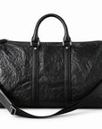 Textured black full-grain leather weekender bag with an adjustable shoulder strap draped across