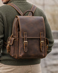 Vintage brown leather backpack for men with adjustable shoulder straps, buckle closure and side pockets, back view