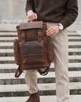 Vintage brown leather backpack for men with large front pocket, side zip pockets, buckle straps and carry handle, front view