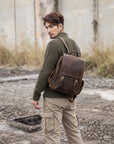 Vintage brown leather backpack for men with buckle straps and side pockets, worn as a travel rucksack outdoors