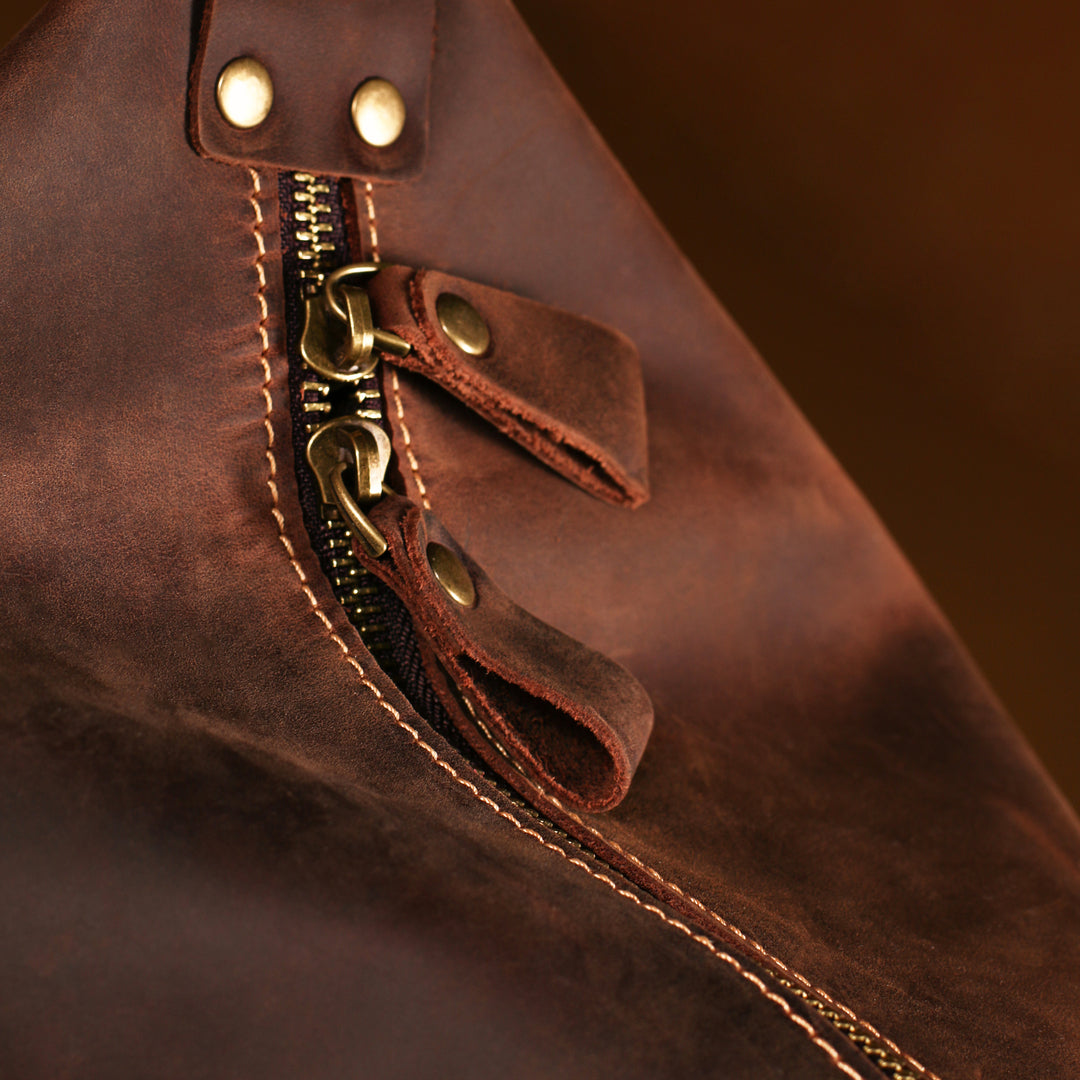 Close-up of high-quality brass zipper pull and stitching on vintage handmade leather travel duffle bag