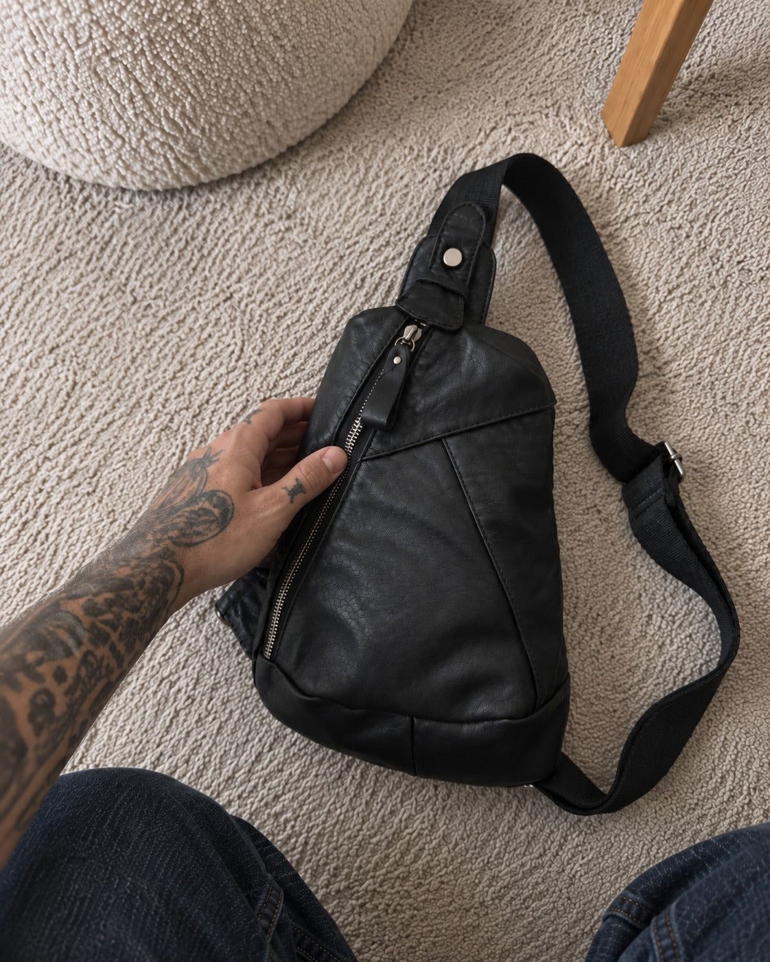 Black leather sling bag with diagonal zipper and adjustable strap, close-up view