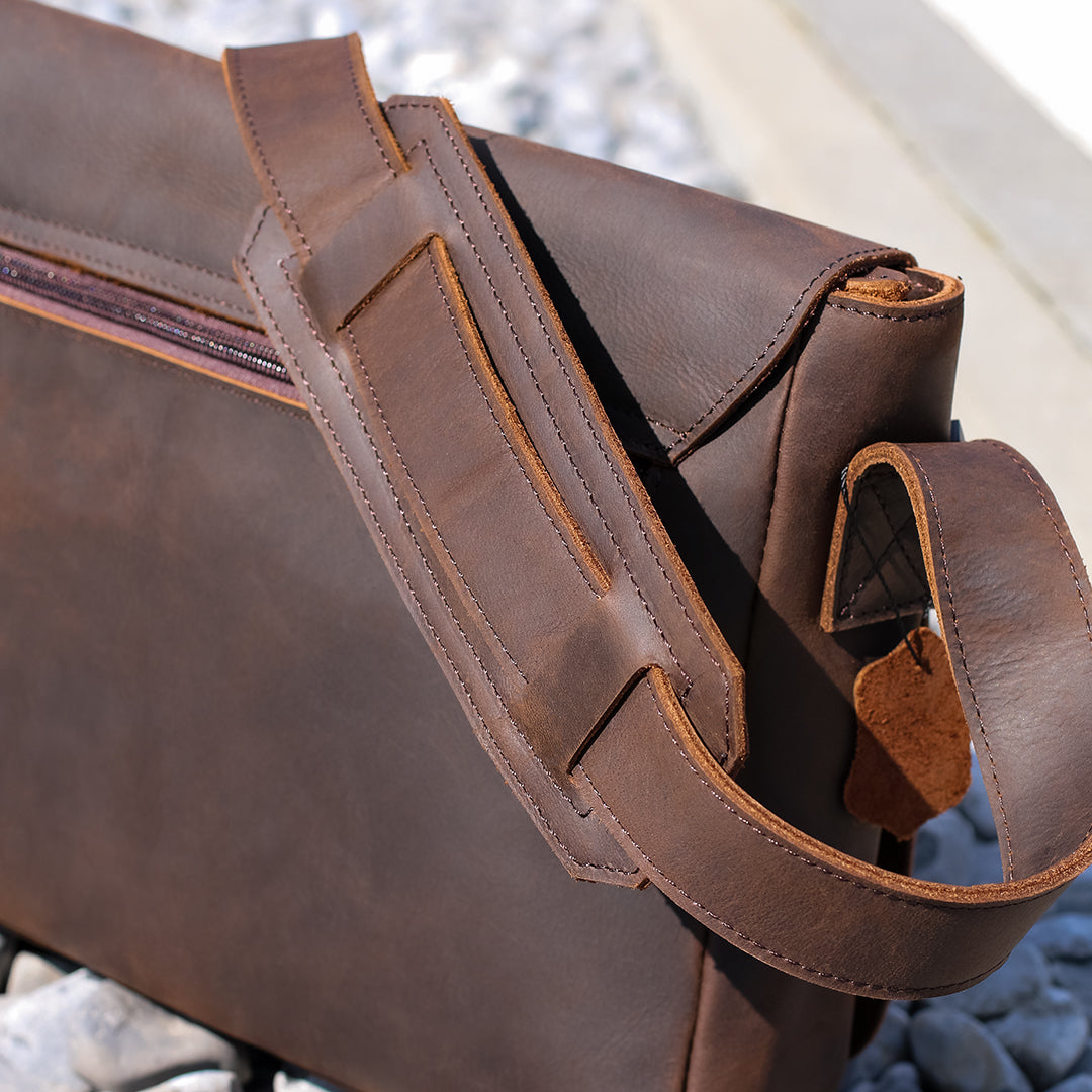 Back view of a men&#39;s dark brown leather shoulder bag with a padded strap and reinforced stitching, designed for comfort.