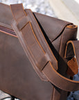 Back view of a men's dark brown leather shoulder bag with a padded strap and reinforced stitching, designed for comfort.