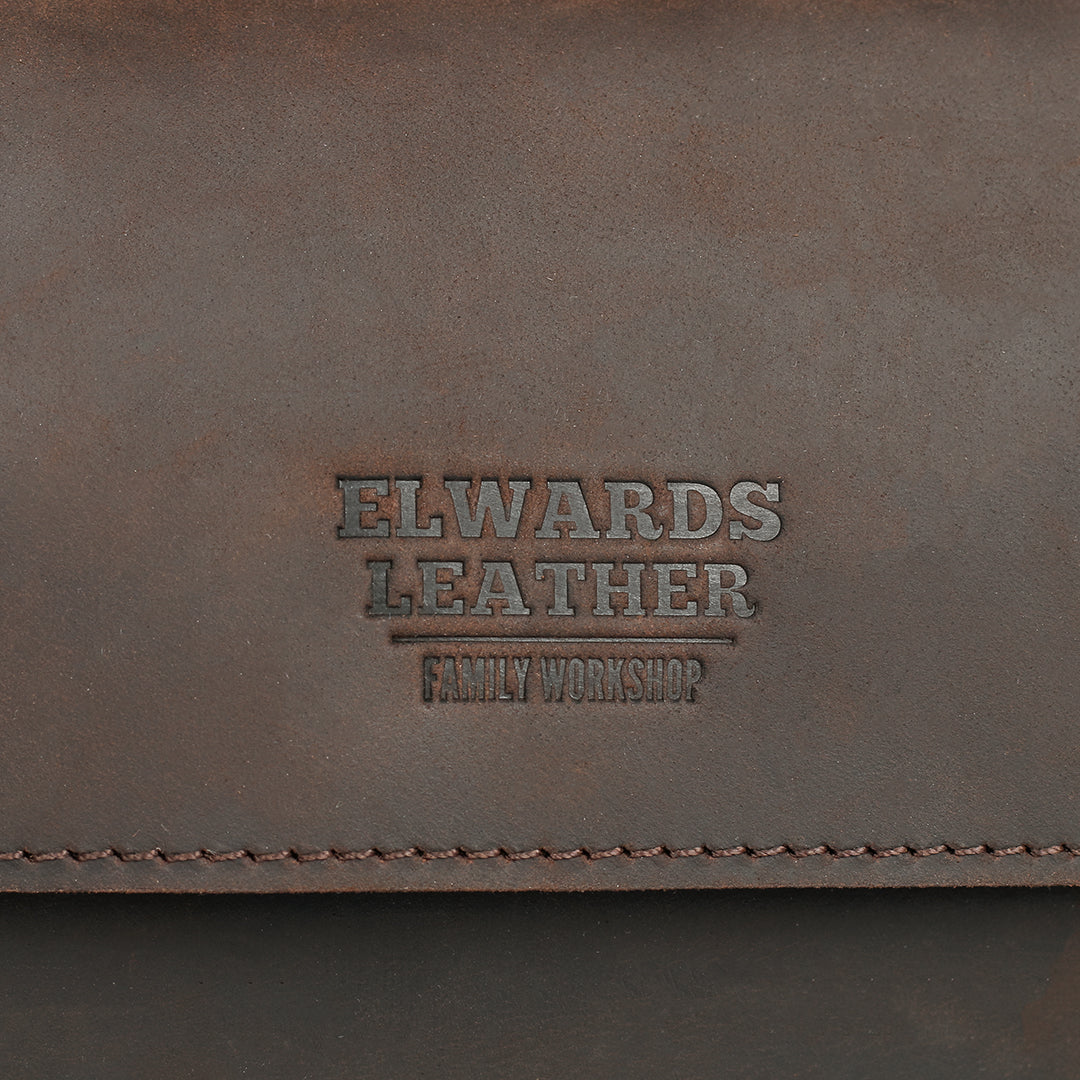 Close-up of the embossed Elwards Leather logo on a dark brown clutch, showcasing refined branding and material texture.