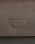 Close-up of the embossed Elwards Leather logo on a dark brown clutch, showcasing refined branding and material texture.