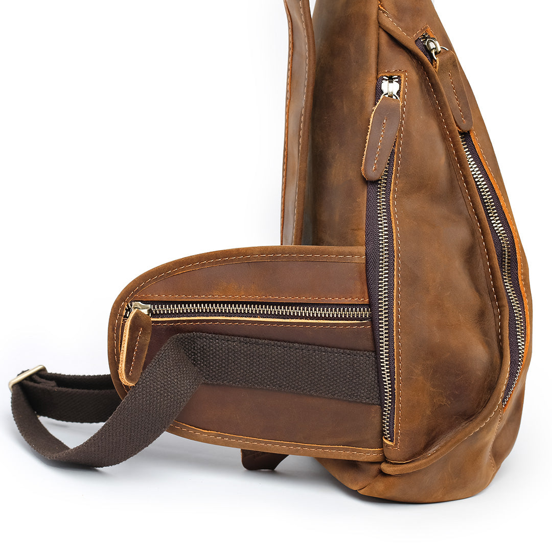 Brown leather sling bag with zippers on a white background