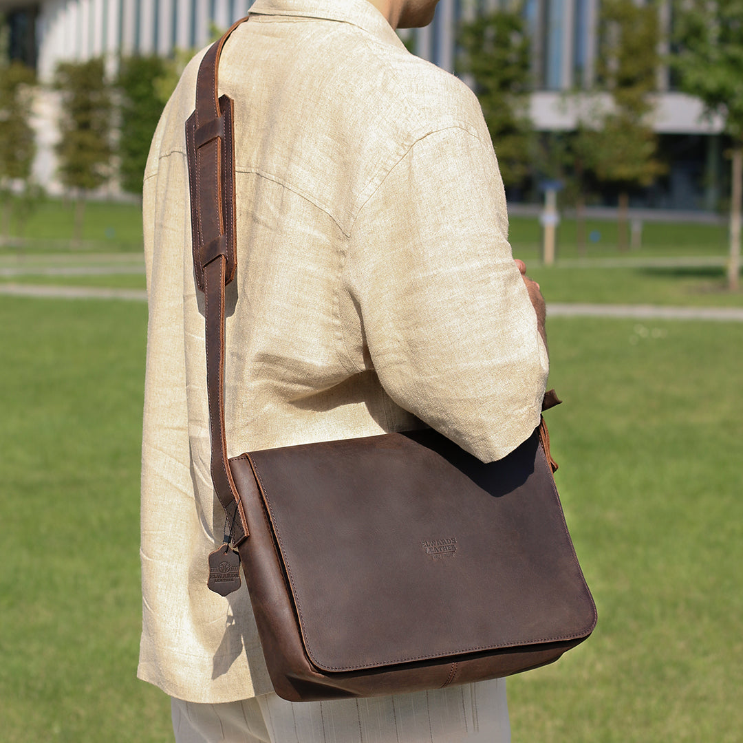 Back view of a dark brown leather satchel bag worn by a model, highlighting padded strap and minimalistic design