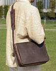 Back view of a dark brown leather satchel bag worn by a model, highlighting padded strap and minimalistic design