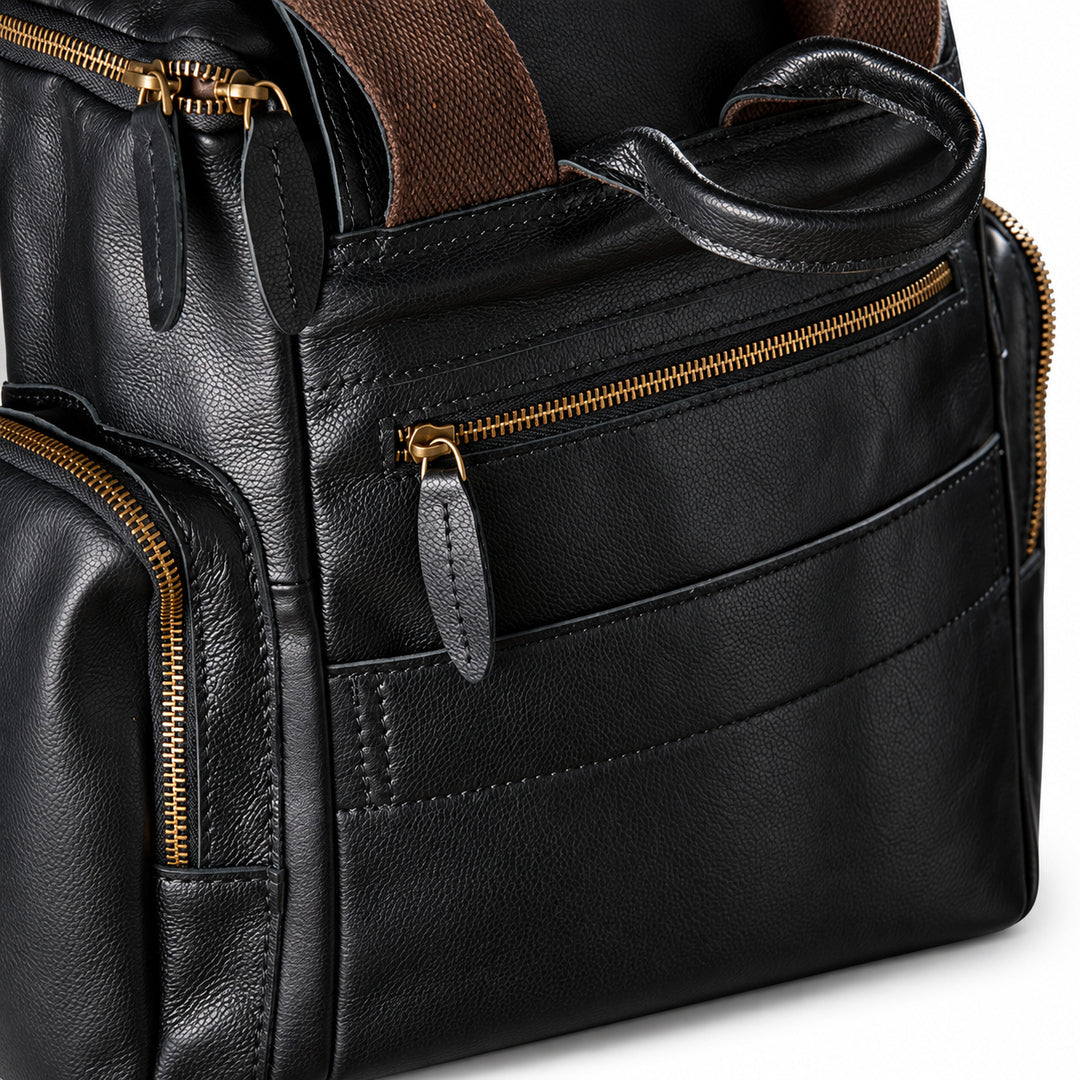 Black full-grain leather backpack top closure with a gold-tone double zipper and leather pulls
