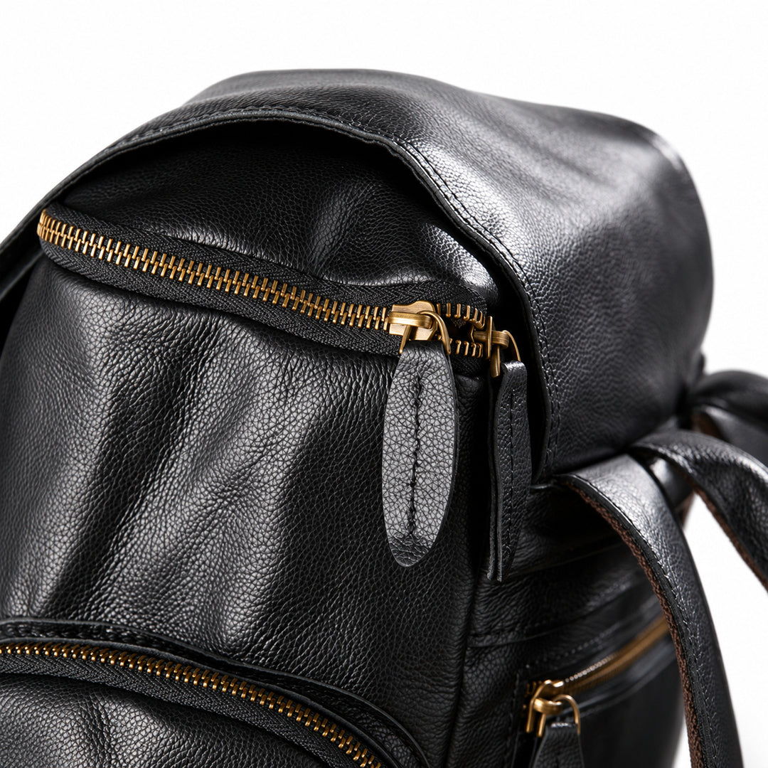 Black full-grain leather backpack top closure with a gold-tone double zipper and leather pulls
