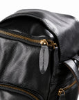 Black full-grain leather backpack top closure with a gold-tone double zipper and leather pulls
