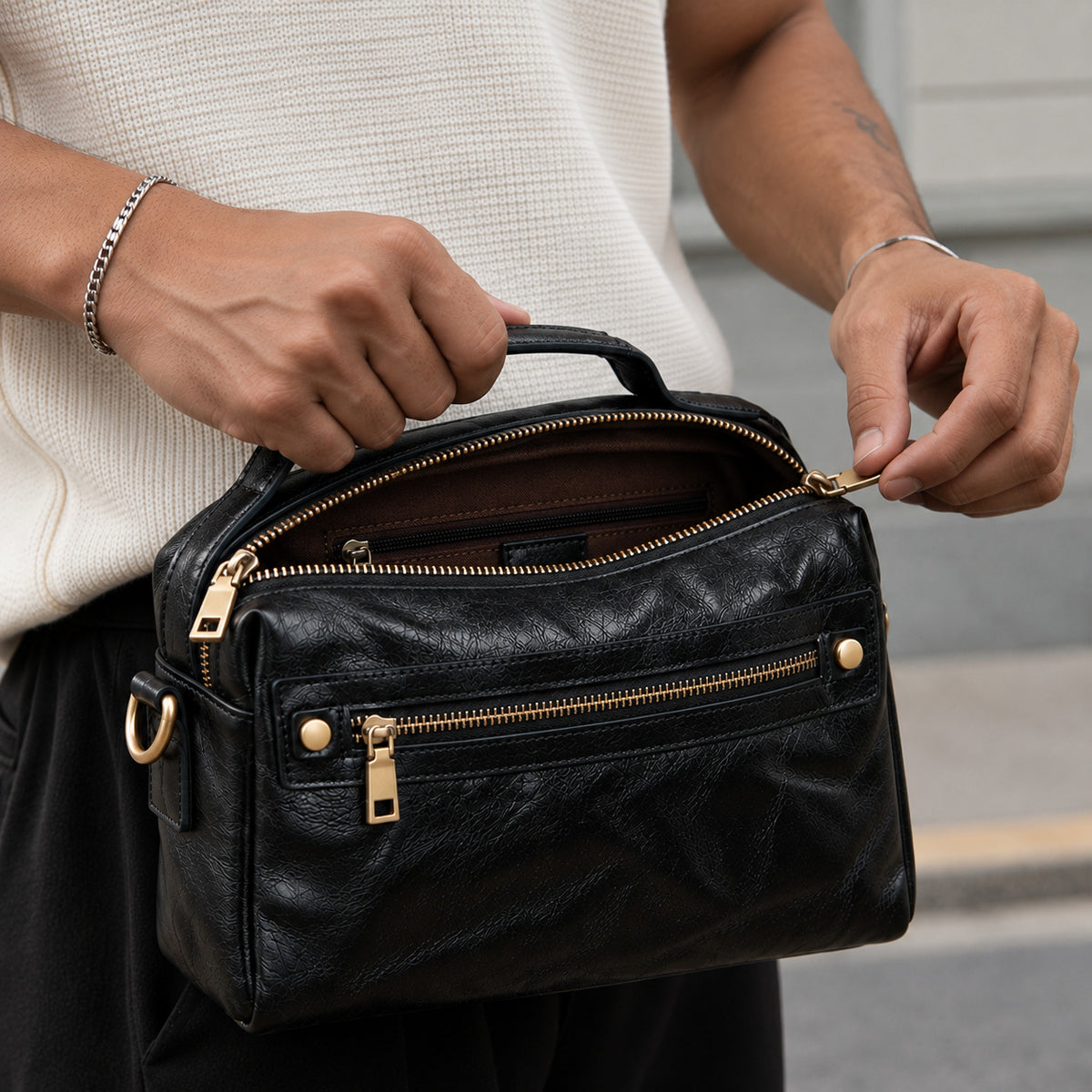 Close-up of a black leather crossbody bag opened to show the zippered main compartment, interior pocket and gold-tone hardware.