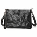 Black leather clutch bag with a crinkled texture, featuring a wristlet strap, top zipper closure, and a detachable shoulder strap.