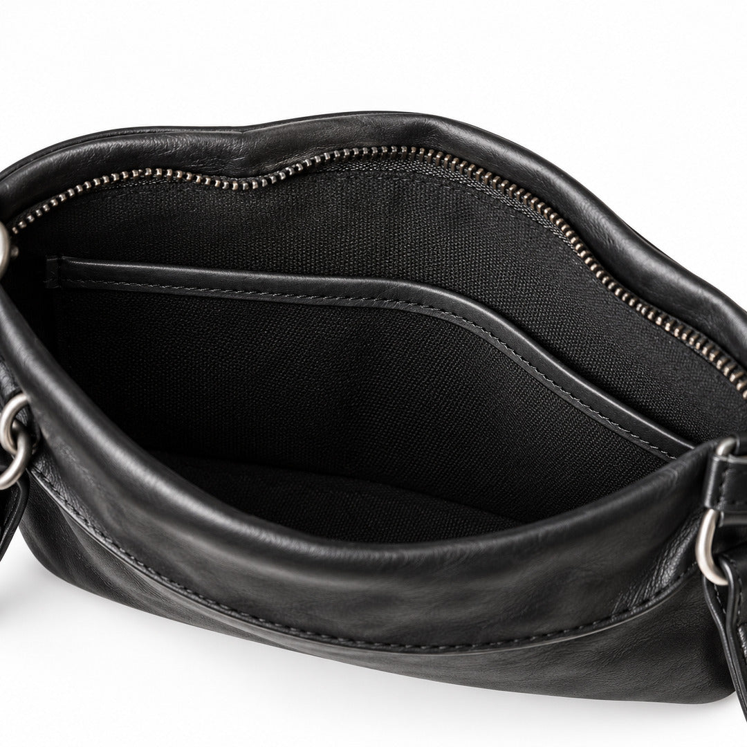 Close-up of the interior of a black leather handbag, showing a zippered opening, black fabric lining, and silver-tone metal hardware.