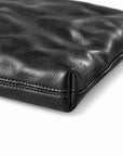 Close-up of a black leather pouch or clutch showing the textured grain and stitched edge.