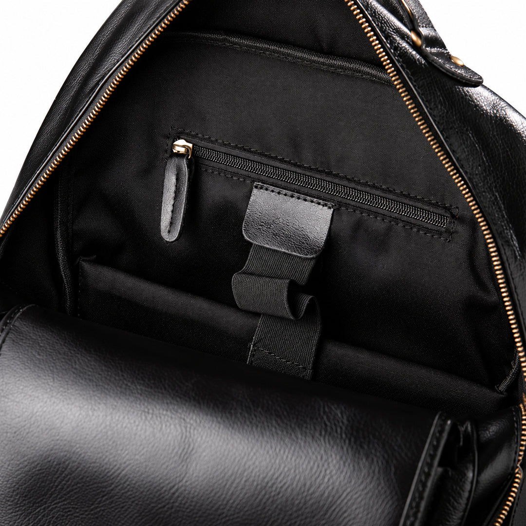 Close-up of the interior of a black leather backpack, showing a black fabric zippered pocket with a gold-tone zipper pull and a black elastic strap.