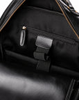 Close-up of the interior of a black leather backpack, showing a black fabric zippered pocket with a gold-tone zipper pull and a black elastic strap.