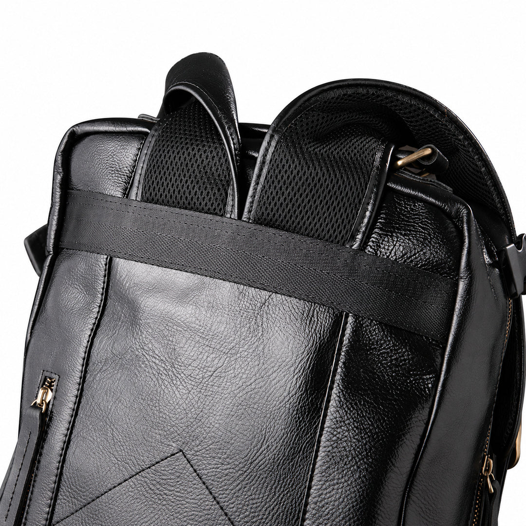 Close-up of a black faux-leather backpack showing the top handle, mesh ventilation panels, and a horizontal compression strap with gold-tone zipper pulls.