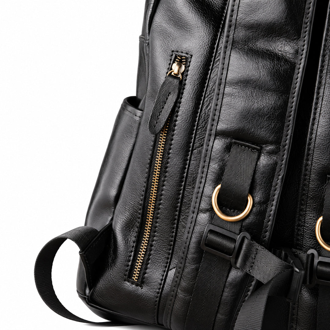 Close-up detail of a black leather backpack showing a vertical zippered pocket with a gold-tone zipper, a side pocket, and gold-tone metal D-ring hardware.