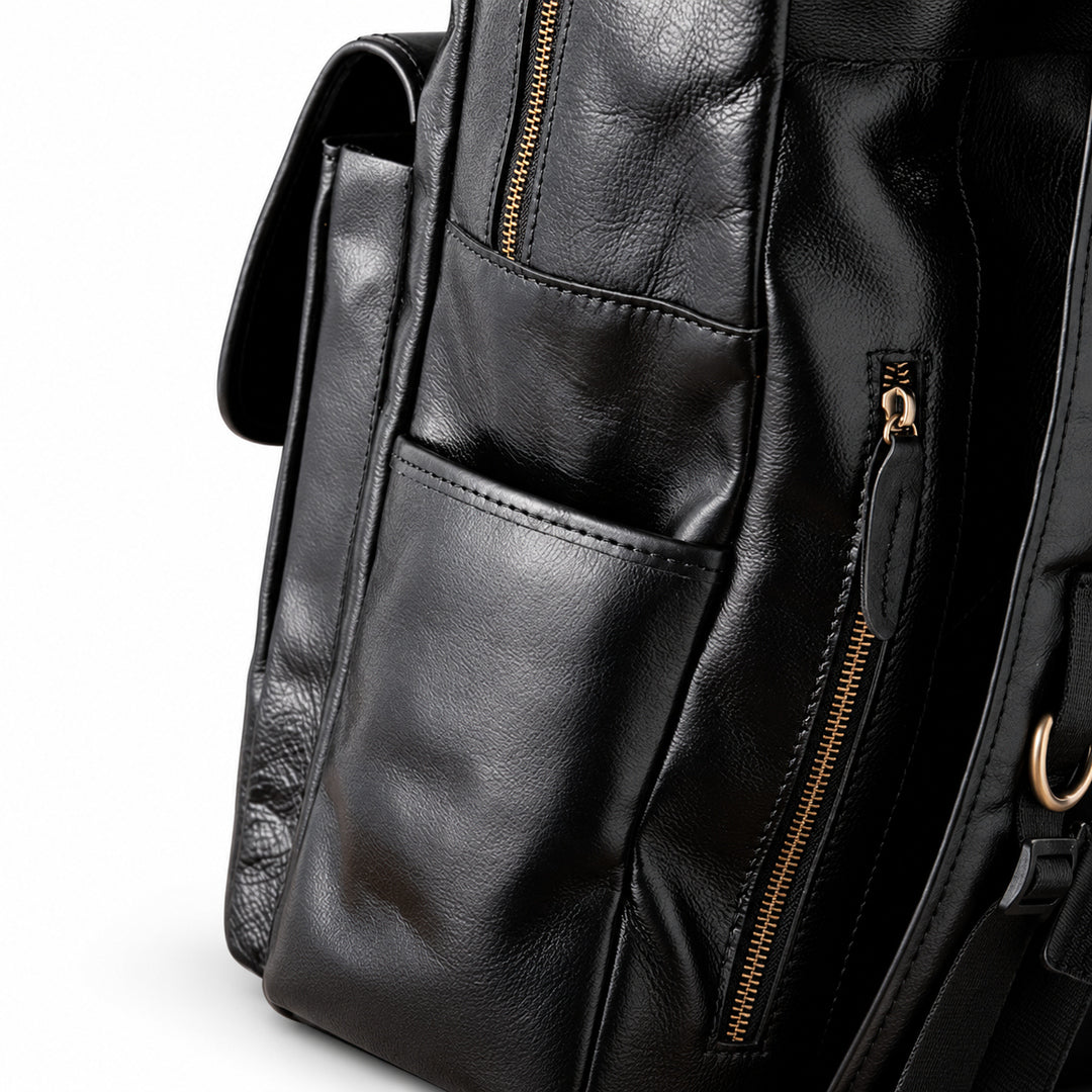 Close-up of a black leather backpack showing a front pocket, side pocket, and gold-tone zipper details.