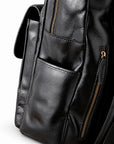 Close-up of a black leather backpack showing a front pocket, side pocket, and gold-tone zipper details.