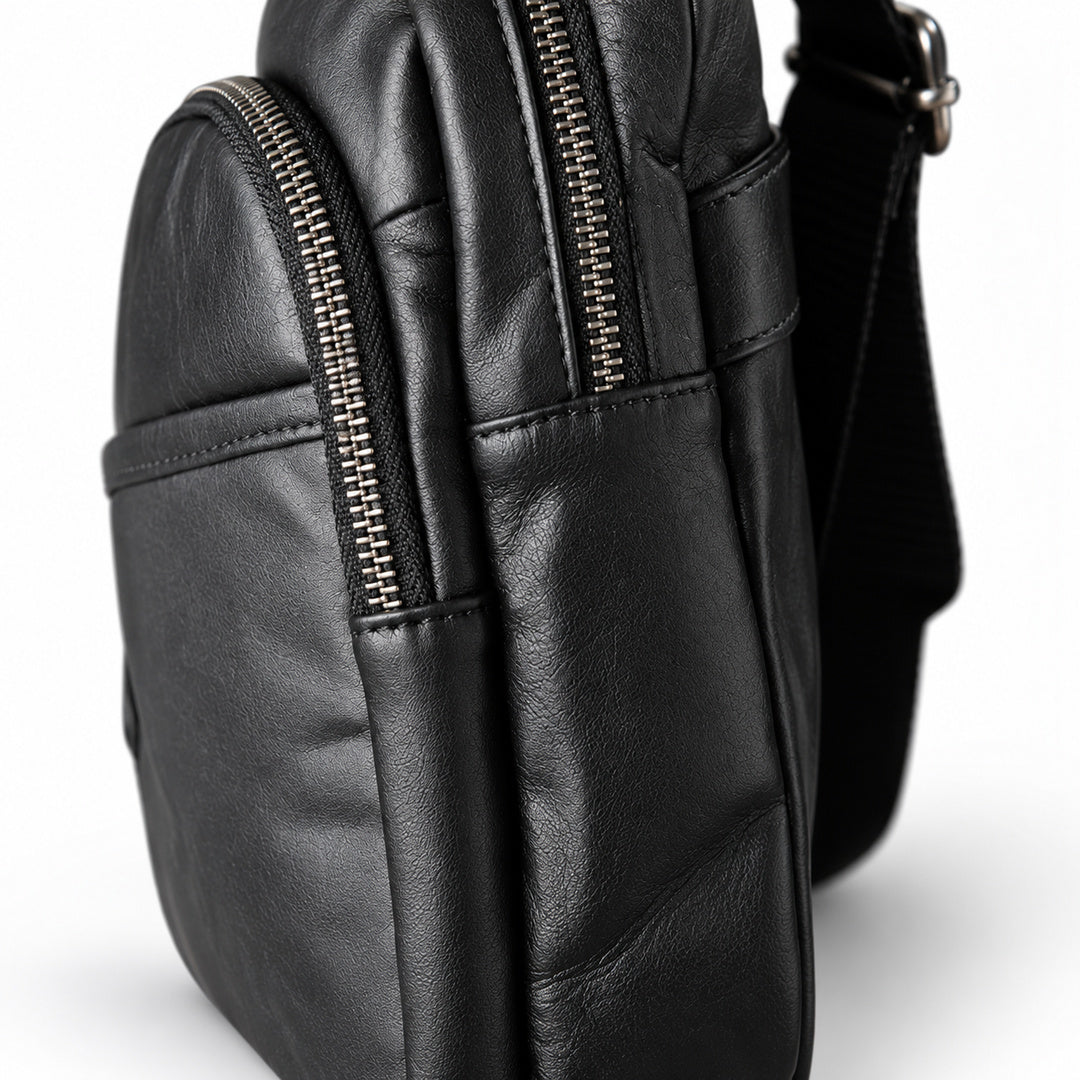 Close-up of two metal zippers with riveted black leather pulls on the sling bag.