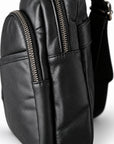 Close-up of two metal zippers with riveted black leather pulls on the sling bag.