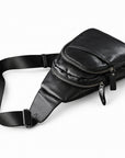 Side view of a black leather sling bag showing two separate zip compartments and the shoulder strap.