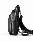 Side view of a black leather sling bag showing two separate zip compartments and the shoulder strap.