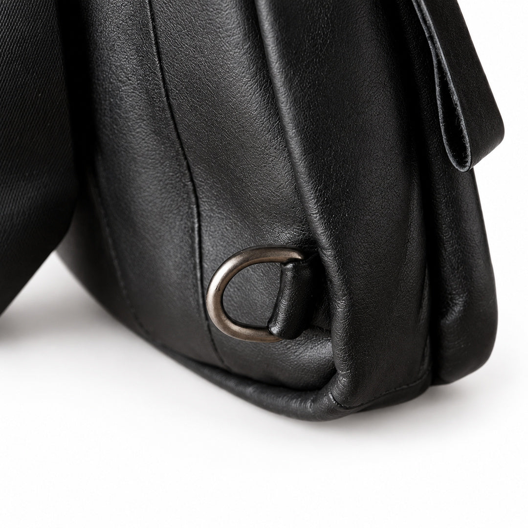 Close-up of a black leather bag corner showing a dark metal D-ring attachment and part of the strap.
